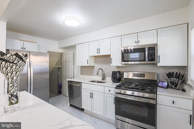 kitchen with white cabinetry, stainless steel appliances, sink, and light stone counters