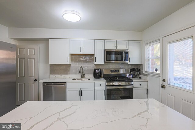 kitchen featuring sink, light stone counters, appliances with stainless steel finishes, white cabinets, and decorative backsplash