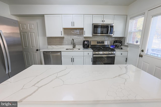 kitchen with stainless steel appliances, sink, light stone countertops, white cabinets, and decorative backsplash