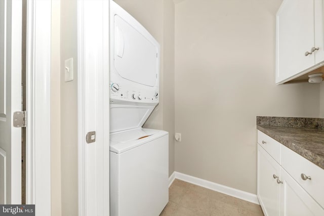 laundry room featuring stacked washer / drying machine, cabinets, and light tile patterned floors