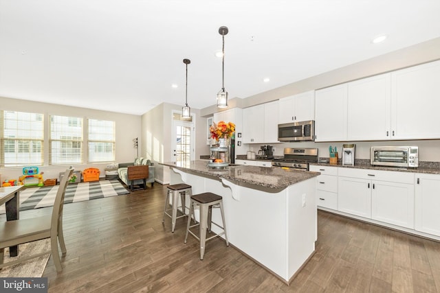 kitchen with dark wood-type flooring, stainless steel appliances, dark stone counters, and a kitchen island