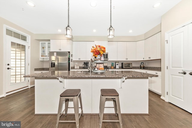 kitchen featuring dark wood-type flooring, dark stone countertops, a center island with sink, white cabinetry, and appliances with stainless steel finishes