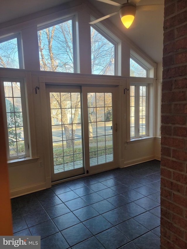 doorway to outside with a wealth of natural light, high vaulted ceiling, and dark tile patterned flooring