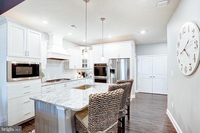 kitchen featuring appliances with stainless steel finishes, sink, decorative light fixtures, white cabinets, and custom range hood