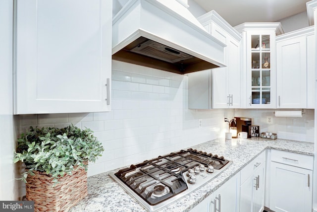 kitchen featuring stainless steel gas stovetop, premium range hood, white cabinetry, and decorative backsplash