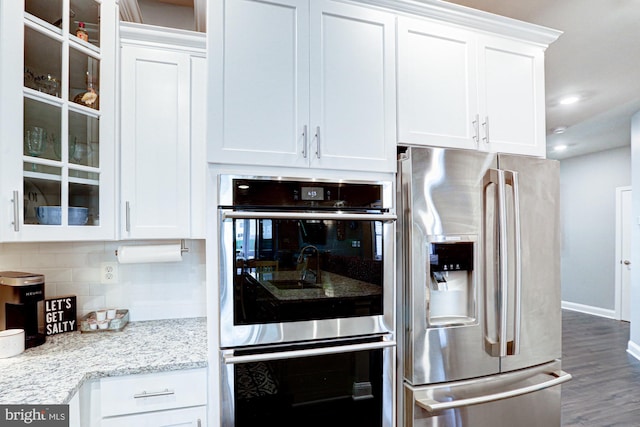 kitchen with tasteful backsplash, white cabinetry, stainless steel appliances, dark wood-type flooring, and light stone counters