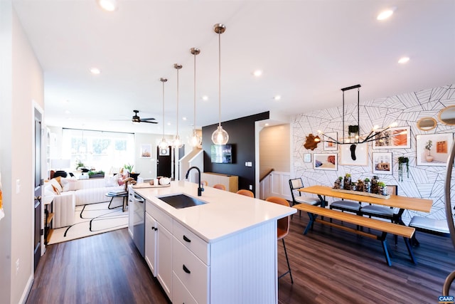 kitchen with sink, an island with sink, hanging light fixtures, white cabinets, and dark wood-type flooring