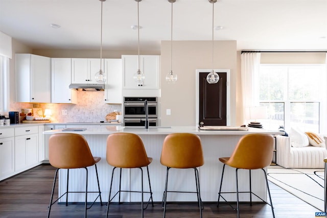 kitchen featuring white cabinetry, double oven, a center island, and hanging light fixtures