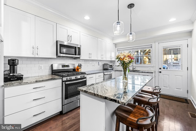 kitchen featuring stainless steel appliances, white cabinetry, light stone counters, dark hardwood / wood-style floors, and a center island