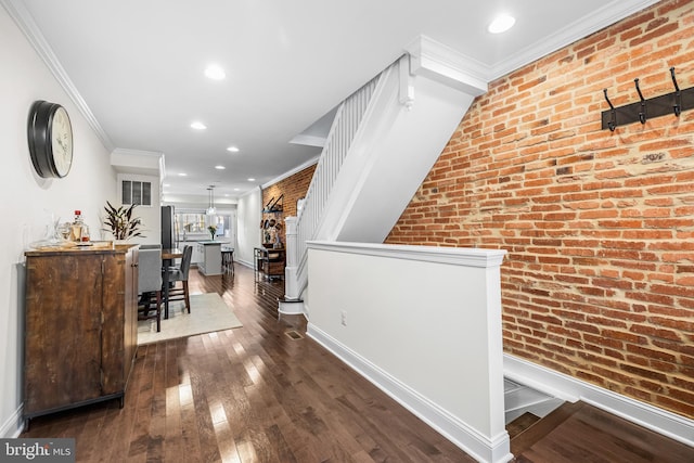 corridor featuring dark wood-type flooring, ornamental molding, and brick wall