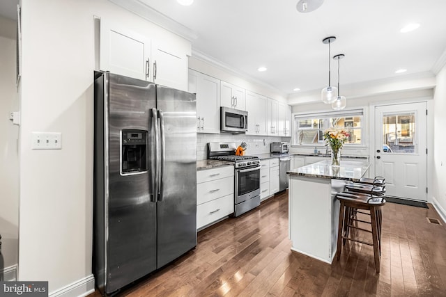 kitchen with white cabinetry, appliances with stainless steel finishes, dark hardwood / wood-style floors, a breakfast bar area, and a kitchen island