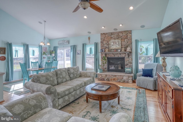 living room with a stone fireplace, light hardwood / wood-style floors, a healthy amount of sunlight, and vaulted ceiling