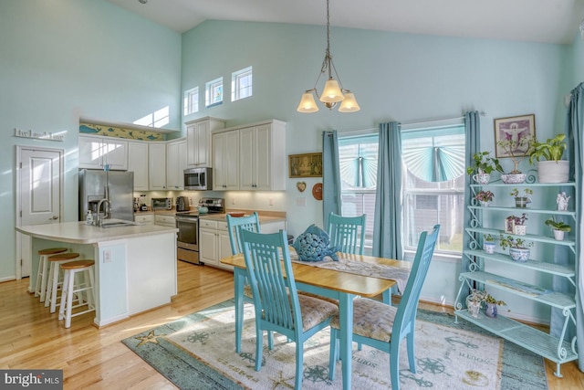 dining room with plenty of natural light, sink, light hardwood / wood-style flooring, and high vaulted ceiling