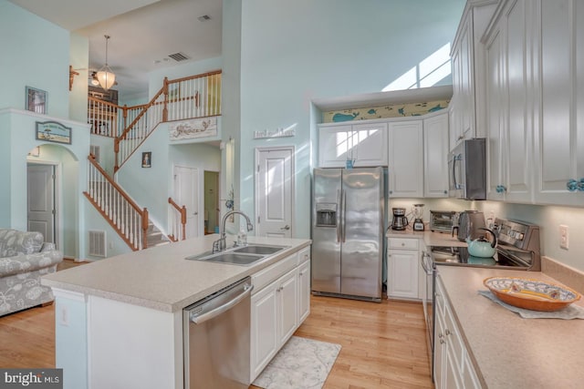 kitchen with stainless steel appliances, sink, light hardwood / wood-style floors, a high ceiling, and a kitchen island with sink