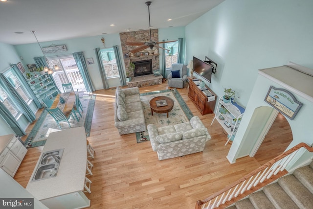 living room featuring light wood-type flooring, a wealth of natural light, ceiling fan with notable chandelier, and a fireplace