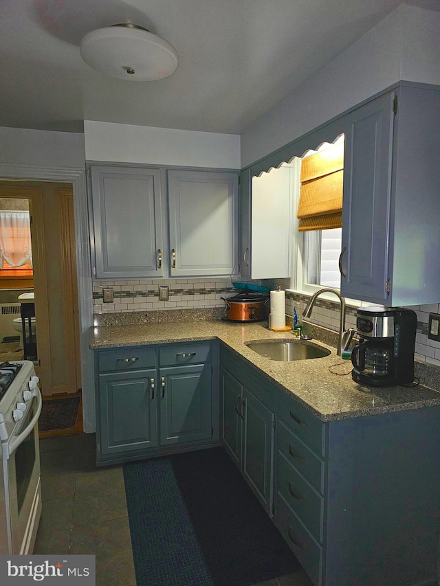 kitchen with backsplash, dark tile patterned floors, sink, and white range with gas cooktop