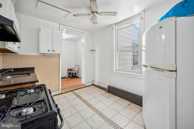 kitchen featuring black range with gas stovetop, backsplash, white cabinetry, range hood, and white refrigerator