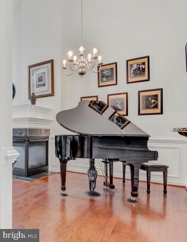 miscellaneous room with a premium fireplace, a notable chandelier, wood-type flooring, and a high ceiling