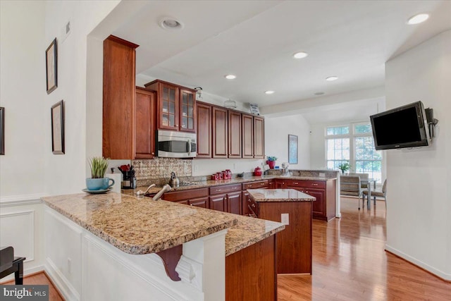 kitchen with a kitchen island, light stone countertops, kitchen peninsula, and light hardwood / wood-style floors