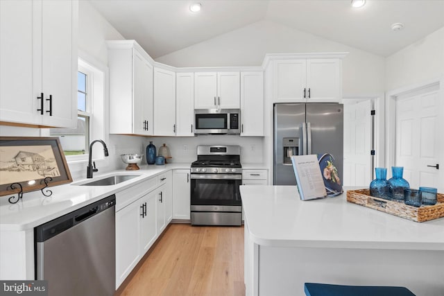 kitchen with sink, vaulted ceiling, stainless steel appliances, and white cabinetry