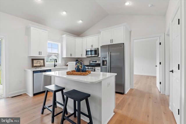 kitchen with white cabinetry, stainless steel appliances, vaulted ceiling, and a kitchen island