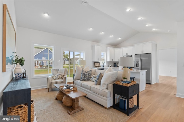 living room with light hardwood / wood-style floors, sink, and vaulted ceiling