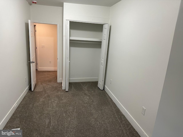 unfurnished bedroom with dark colored carpet and a closet