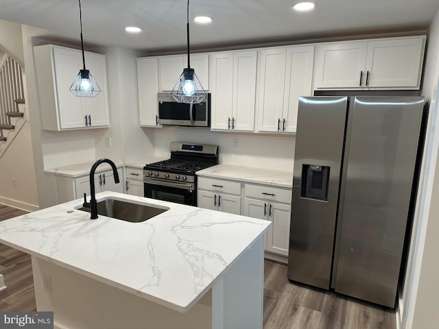 kitchen featuring appliances with stainless steel finishes, light stone countertops, hanging light fixtures, an island with sink, and white cabinets