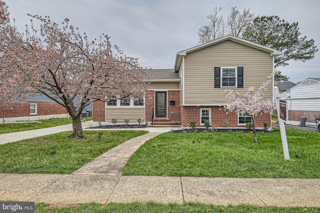 tri-level home with brick siding, a shingled roof, and a front yard