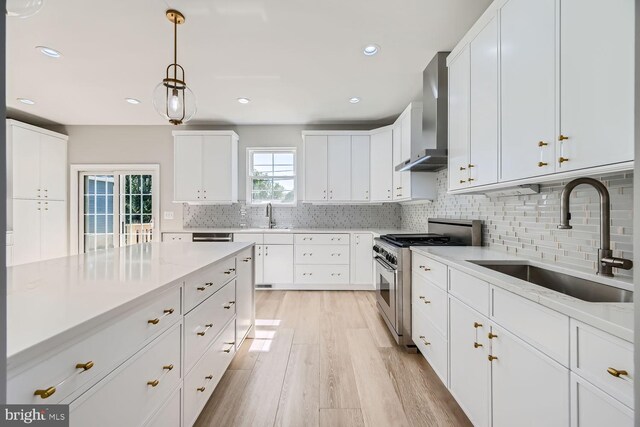 kitchen with high end stove, sink, white cabinetry, and wall chimney range hood