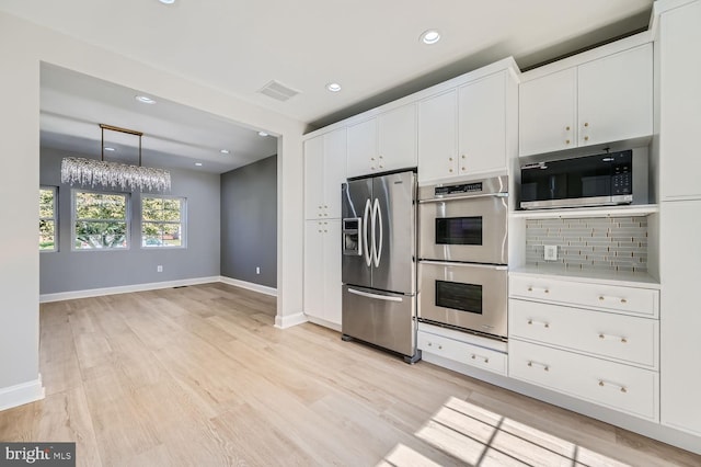 kitchen featuring white cabinets, tasteful backsplash, a chandelier, light hardwood / wood-style floors, and stainless steel appliances