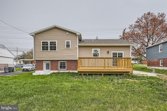 back of house featuring a lawn, brick siding, roof with shingles, and a deck