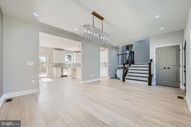 unfurnished living room with an inviting chandelier and light wood-type flooring