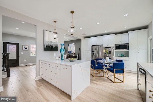 kitchen with appliances with stainless steel finishes, tasteful backsplash, hanging light fixtures, white cabinetry, and light wood-style flooring