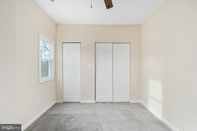 unfurnished bedroom with light carpet, ceiling fan, and two closets