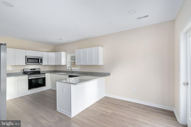 kitchen with a wealth of natural light, light hardwood / wood-style flooring, white cabinets, and appliances with stainless steel finishes