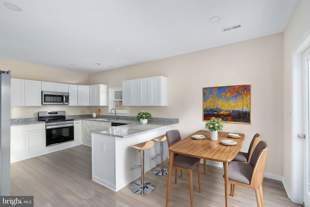 kitchen with kitchen peninsula, light wood-type flooring, light stone counters, stainless steel appliances, and white cabinets