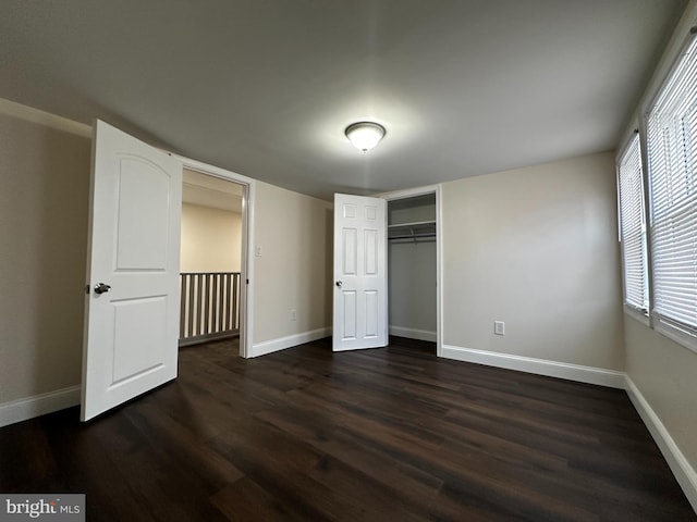 unfurnished bedroom featuring a closet, multiple windows, and dark hardwood / wood-style floors