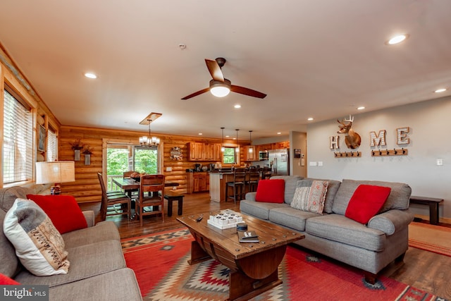 living room with log walls, dark wood-type flooring, and ceiling fan with notable chandelier