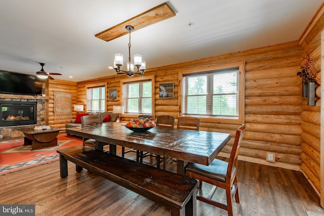 dining space featuring ceiling fan with notable chandelier, rustic walls, wood-type flooring, and a fireplace