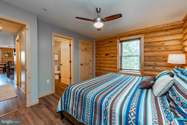 bedroom featuring ensuite bath, dark hardwood / wood-style flooring, rustic walls, and ceiling fan