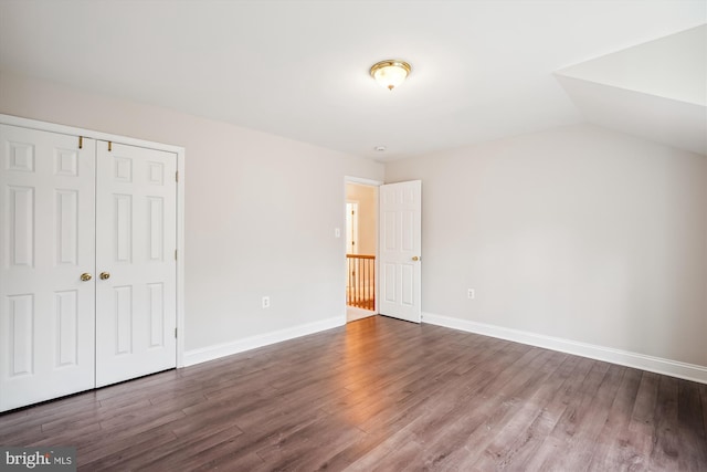 unfurnished bedroom featuring dark hardwood / wood-style flooring, vaulted ceiling, and a closet