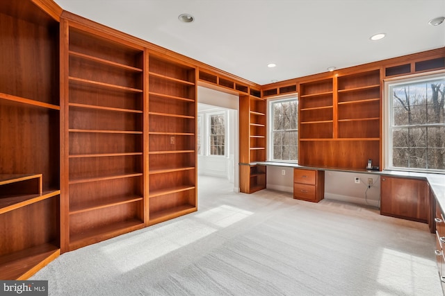 unfurnished office with built in shelves, light colored carpet, and built in desk