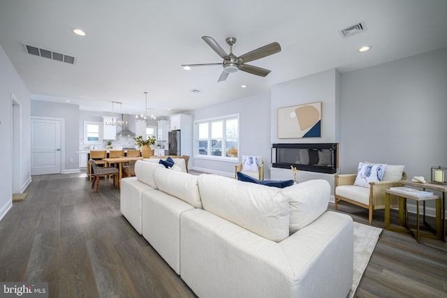 living room with ceiling fan with notable chandelier and dark hardwood / wood-style floors