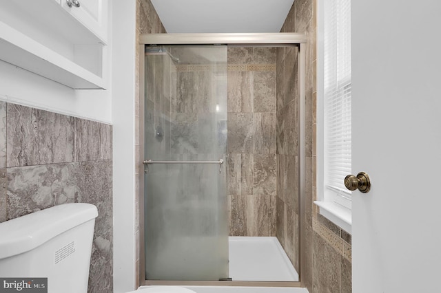 bathroom featuring toilet, tile walls, and a shower with shower door