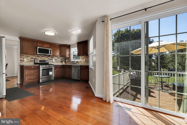 kitchen featuring backsplash, stainless steel appliances, light stone counters, and light hardwood / wood-style flooring