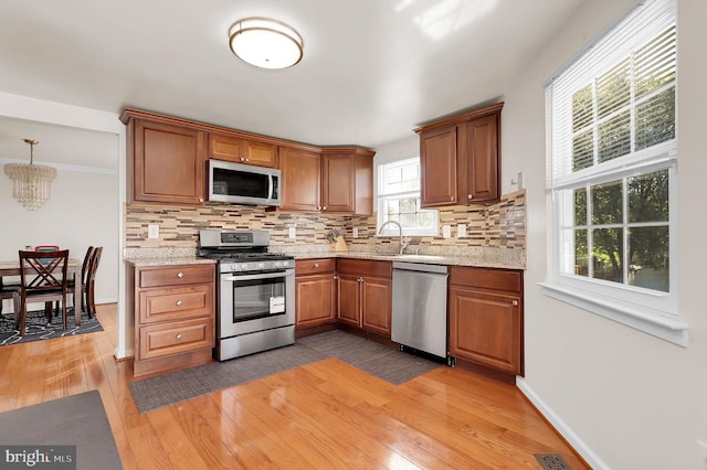 kitchen with appliances with stainless steel finishes, light wood-type flooring, tasteful backsplash, and decorative light fixtures