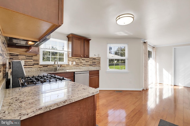 kitchen with light stone countertops, sink, backsplash, light hardwood / wood-style floors, and appliances with stainless steel finishes