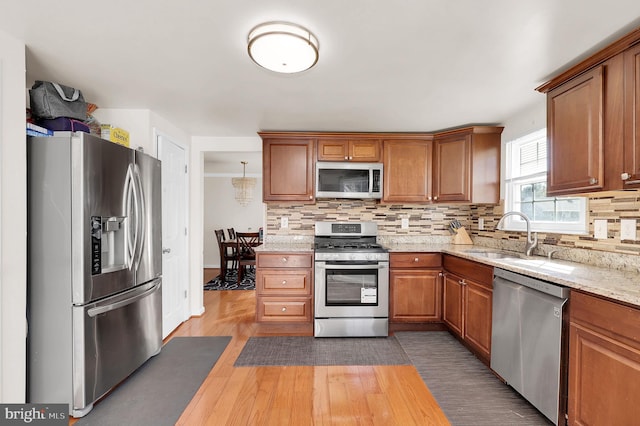 kitchen with sink, decorative backsplash, light stone countertops, light wood-type flooring, and stainless steel appliances