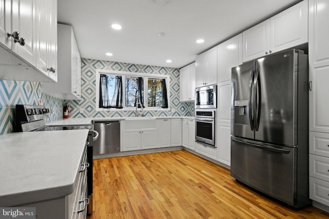 kitchen featuring sink, stainless steel appliances, decorative backsplash, white cabinets, and light wood-type flooring